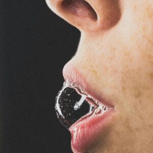 Artistic close-up of a woman blowing a soap bubble on a black background.