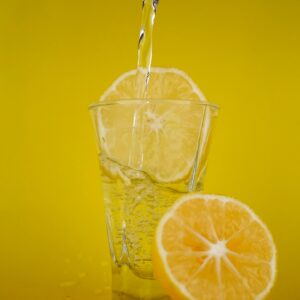 A close-up of water pouring into a glass with lemon slices, vibrant yellow backdrop.
